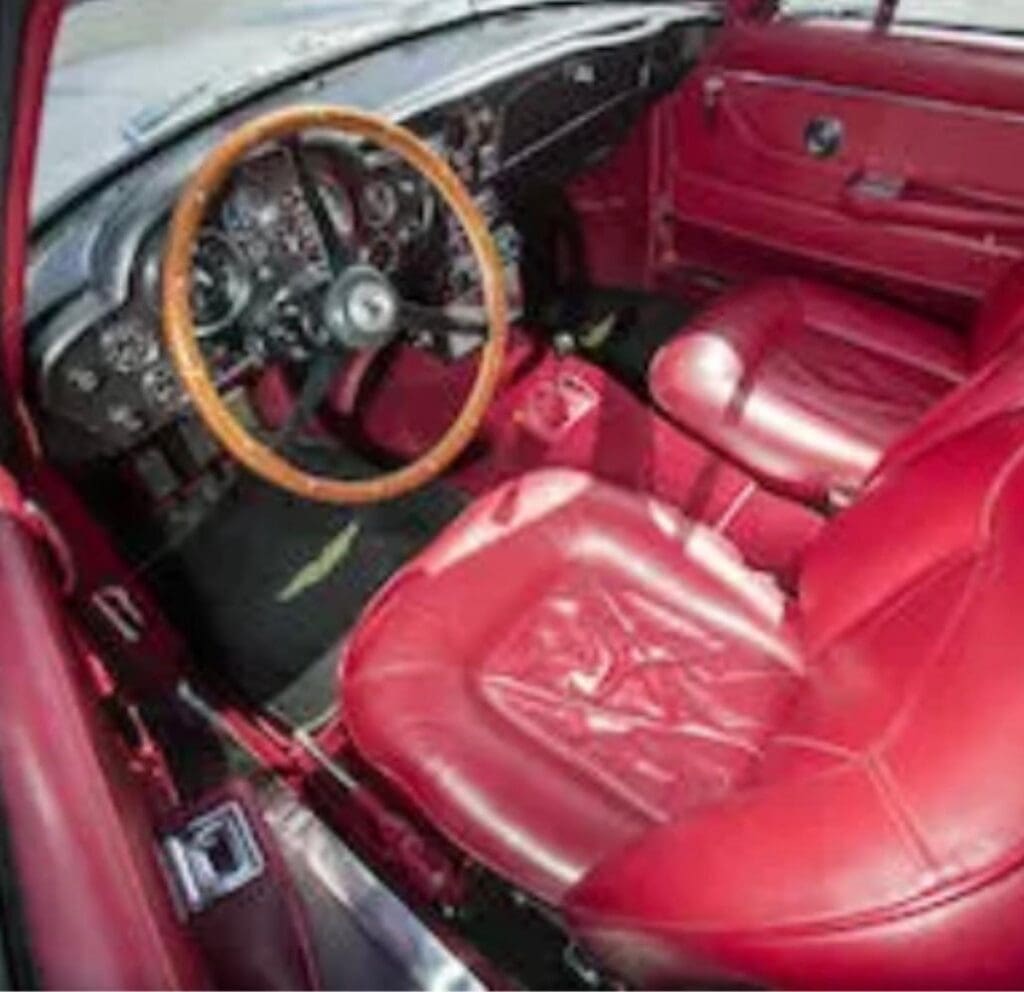 Classic car interior with red leather seats and wooden steering wheel.