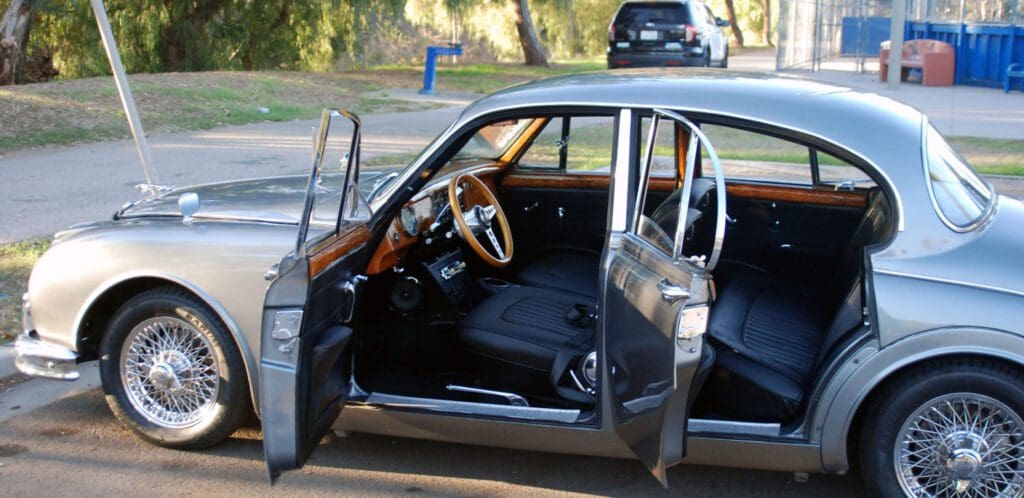 Open car doors revealing a classic black interior with a wooden steering wheel.