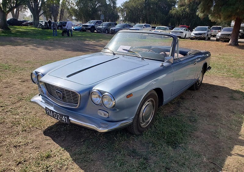 Classic silver convertible car parked on grass in daylight.