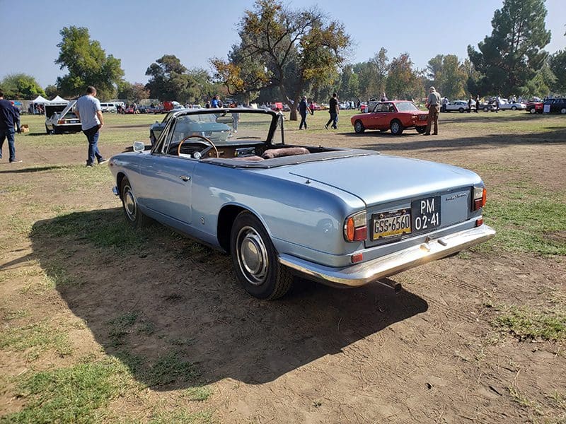 Classic silver convertible car parked on grass in daylight.