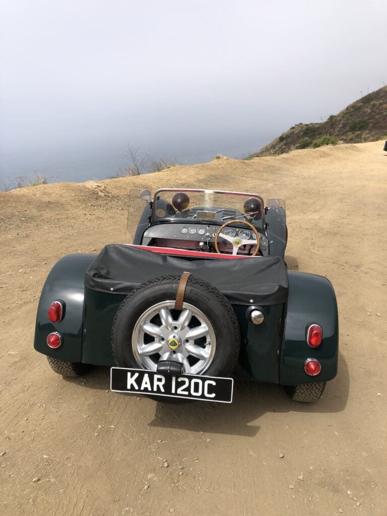 Classic convertible car parked on a dirt road by the coast.