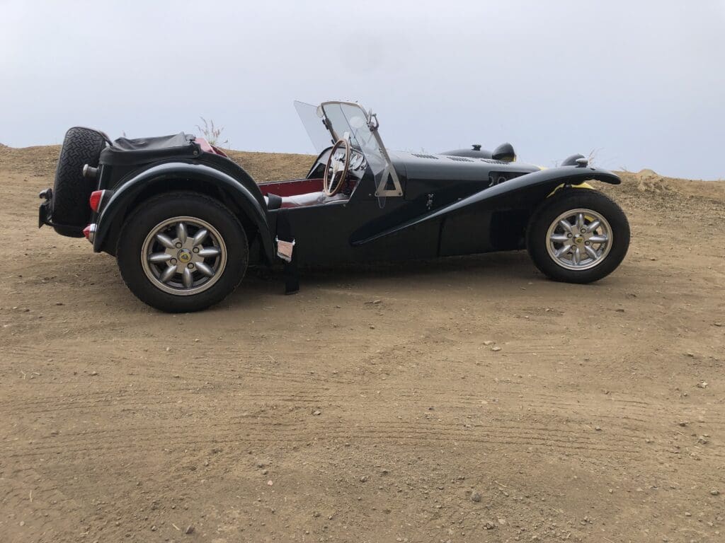 Classic black vintage roadster car parked on a dirt surface.