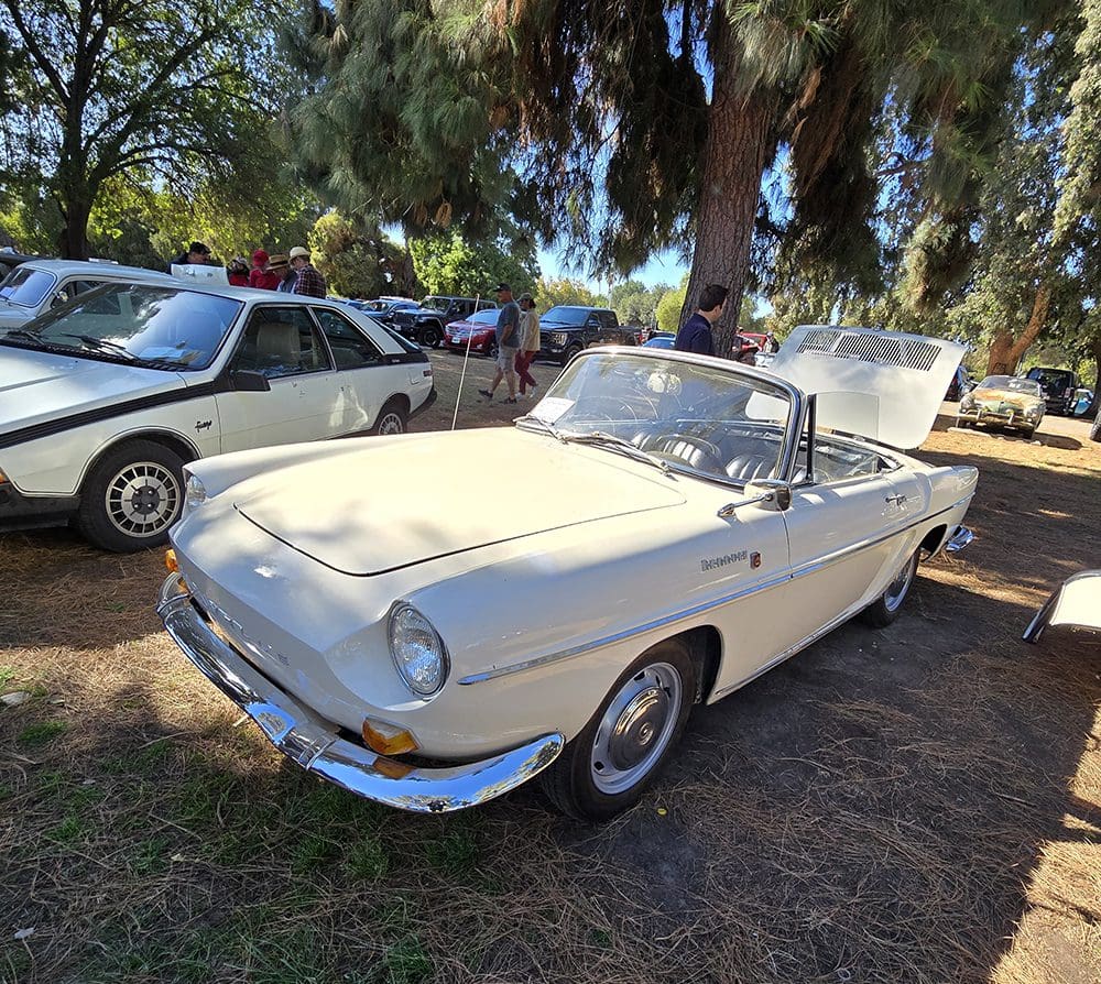 Classic white convertible car parked outdoors among other vintage cars.
