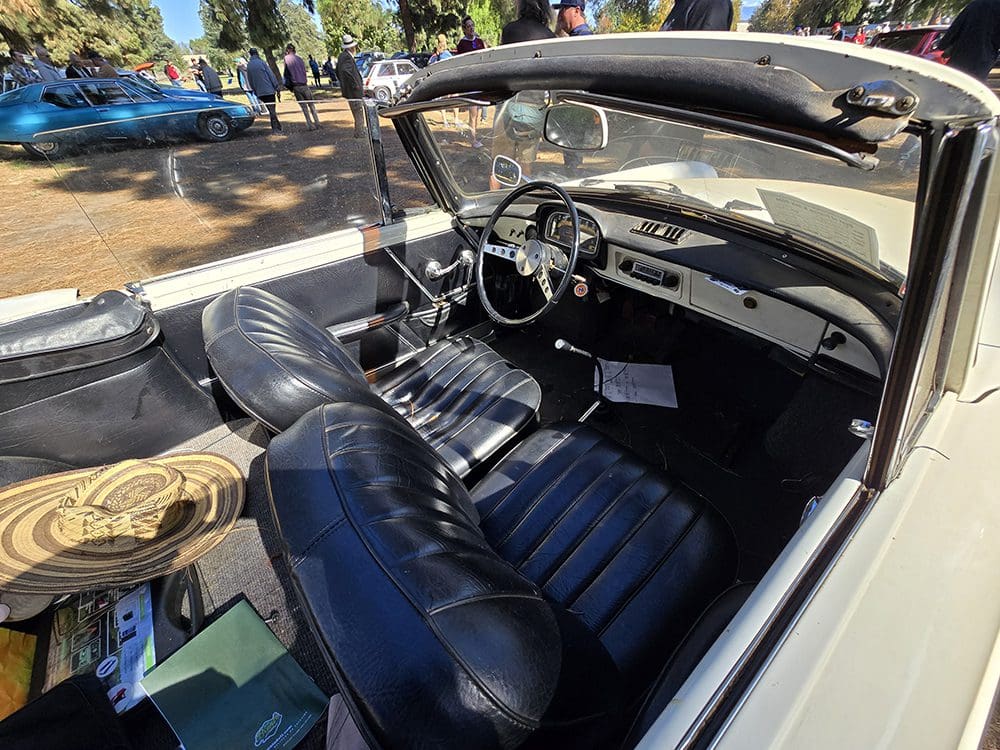 Interior of a classic convertible car with black leather seats and vintage dashboard.