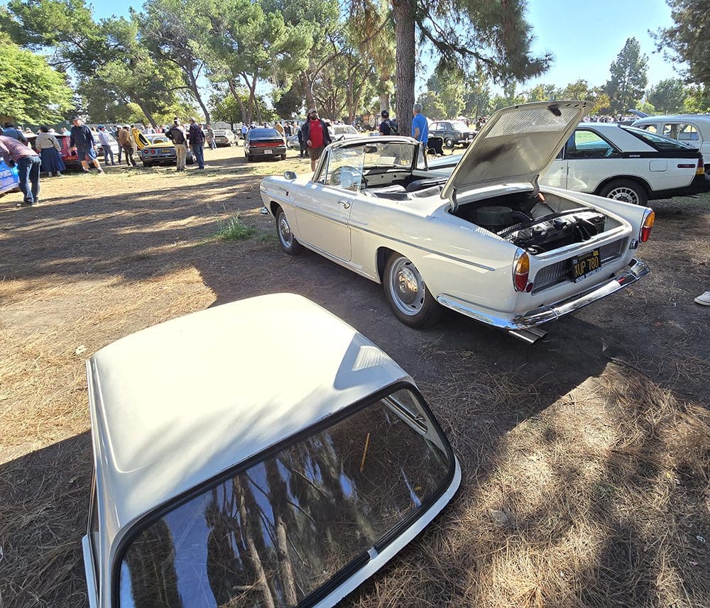 Classic cars displayed at an outdoor car show with open hoods and trunks.
