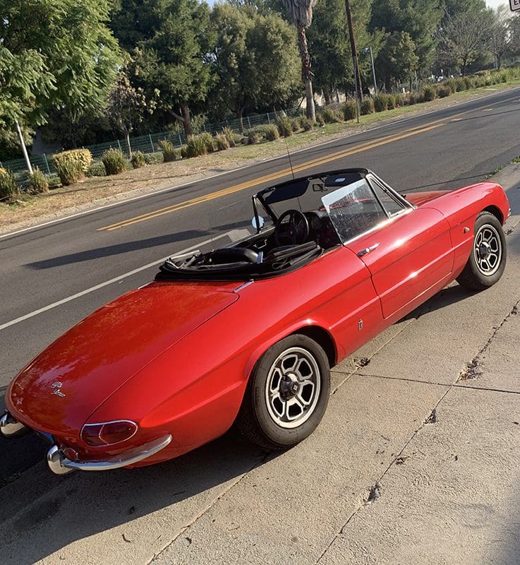 Classic red convertible sports car parked by the roadside.