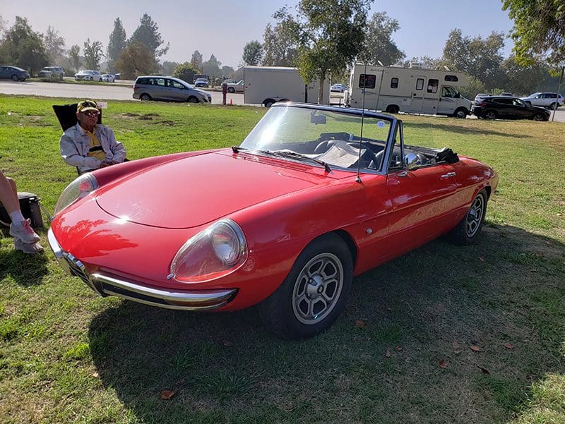 Classic red convertible parked on grass under a clear sky.