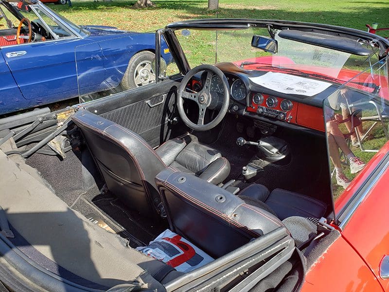 Interior of a vintage convertible car with a red dashboard and black seats.