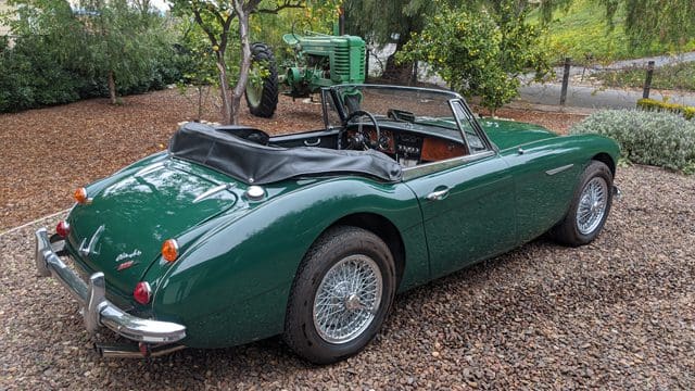 A classic green convertible sports car parked outdoors on gravel.