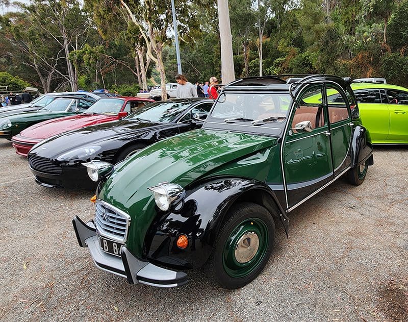 Classic green Citroën 2CV parked among other vintage cars.