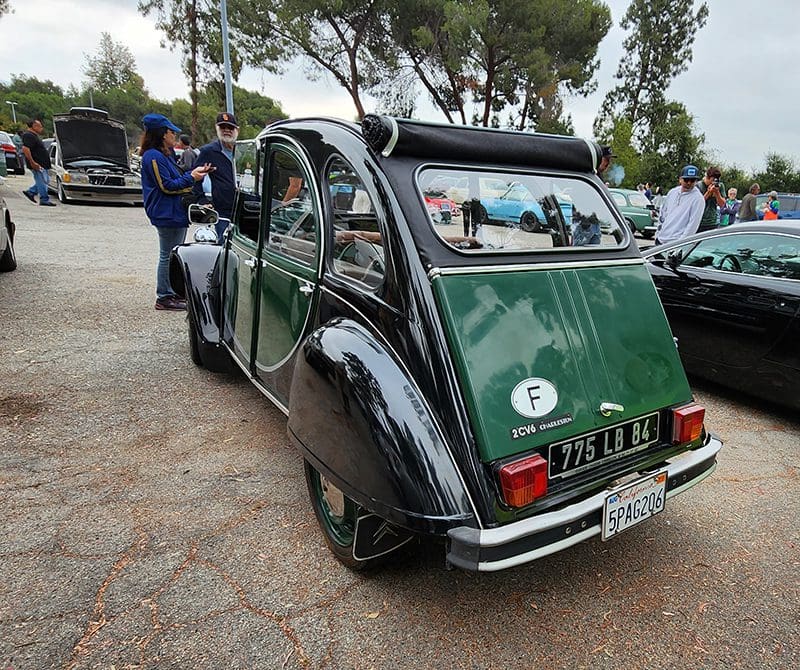 Vintage green and black car at a classic car event with people admiring it.