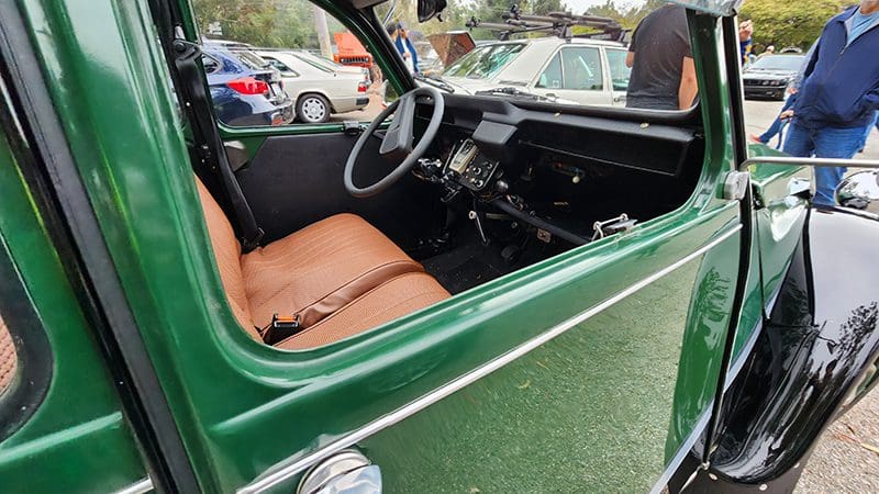 Interior view of a vintage green car with a brown leather seat and classic steering wheel.