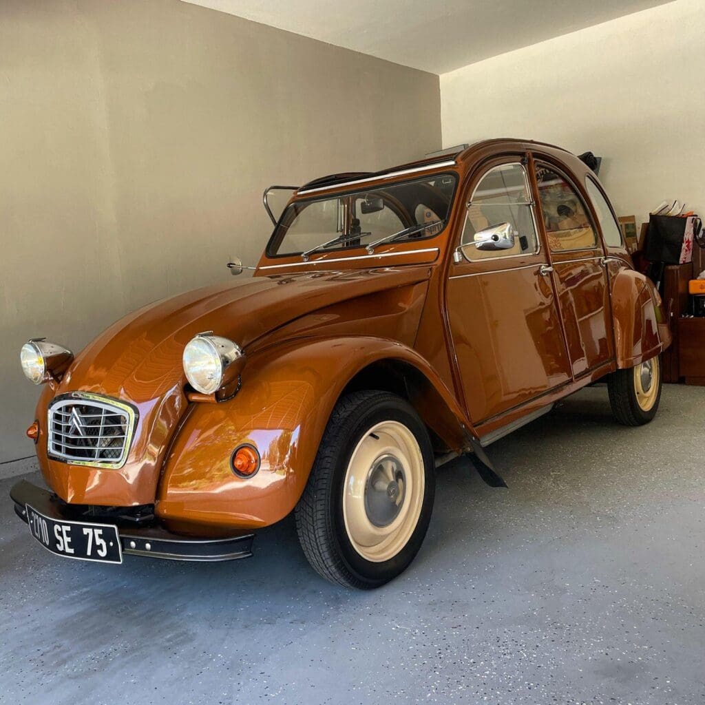 Vintage brown Citroën 2CV parked indoors with beige tires.