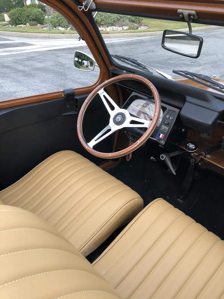 Interior view of a classic car with tan leather seats and a wooden steering wheel.