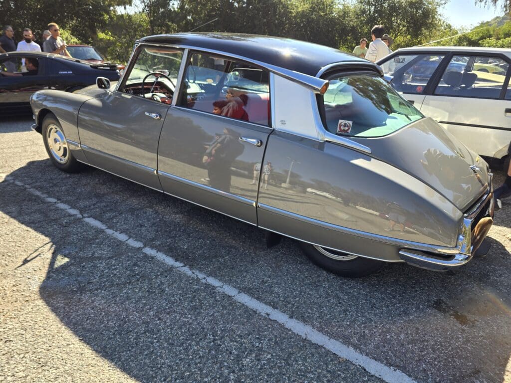 A vintage silver car parked outdoors with a scenic background.