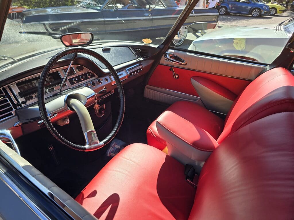 Classic car interior with red leather seats and vintage steering wheel.