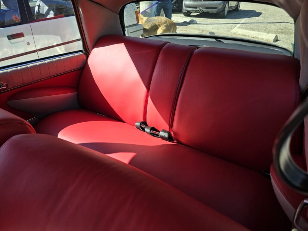Red leather car backseat with seatbelts and sunlight.