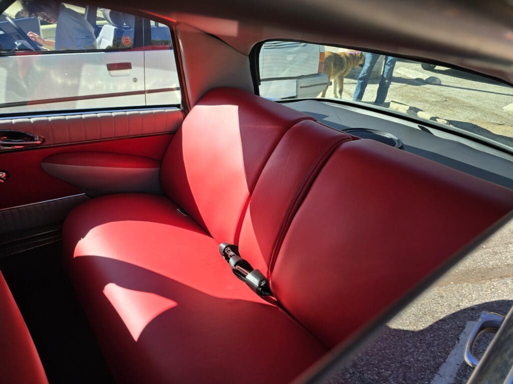 Red leather backseat of a vintage car with seat belts.