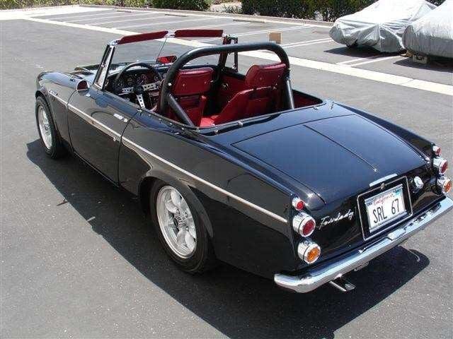 Classic black convertible sports car with red interior parked outdoors.