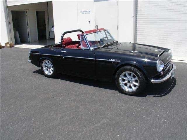 Classic black convertible sports car parked in front of a white building.