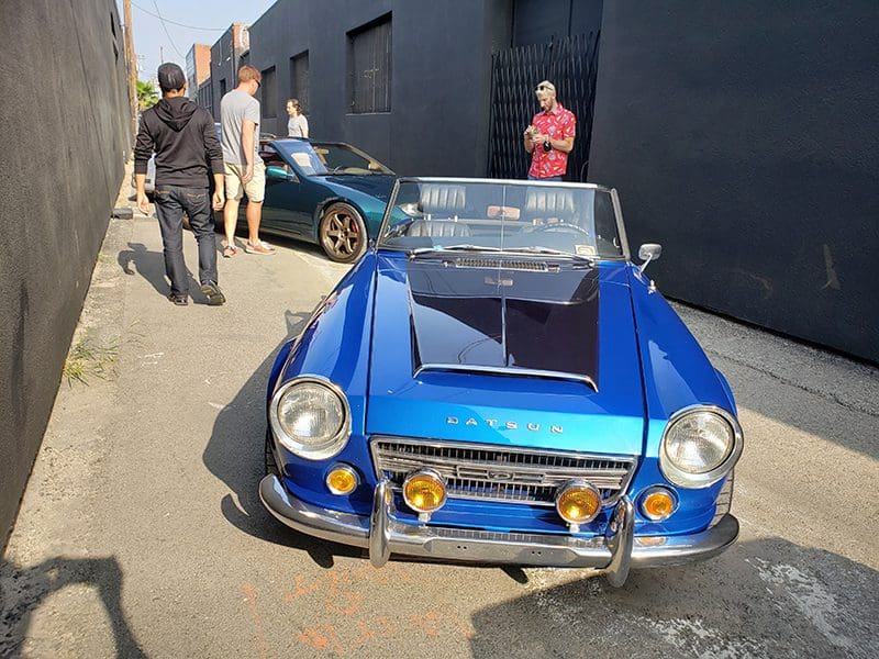 A vintage blue convertible car parked on a street with people around.