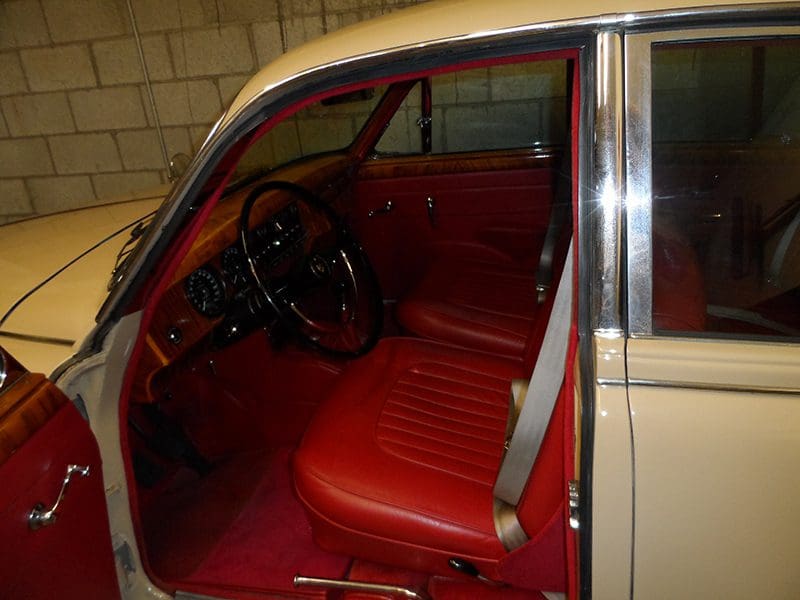Classic car interior with red leather seats and vintage steering wheel.