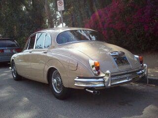 Classic beige vintage car parked on a sunny road with trees.