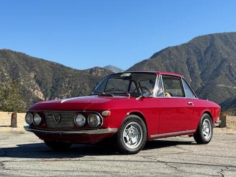 Classic red convertible car parked with mountains in the background.