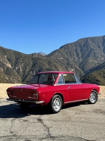 Classic red convertible car parked with mountains in the background.