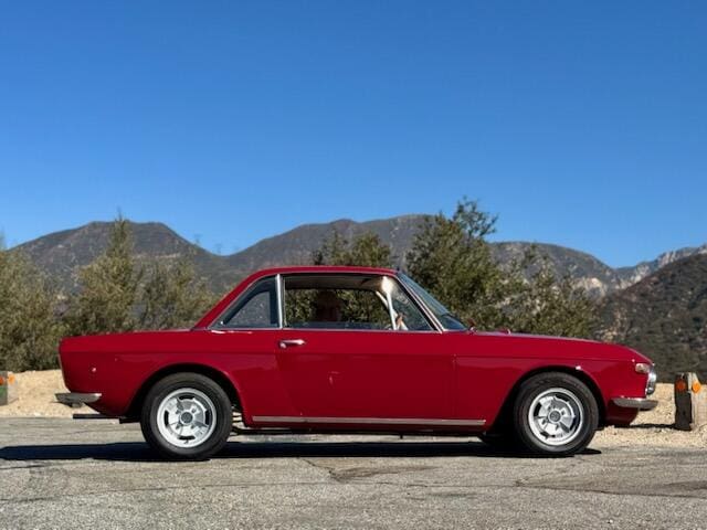 Classic red vintage car parked with mountains in the background.