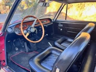 Classic car interior with wooden steering wheel and leather seats.