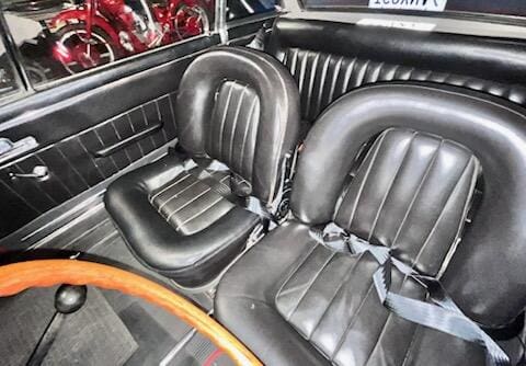 Interior of a vintage car with black leather seats and wooden steering wheel.