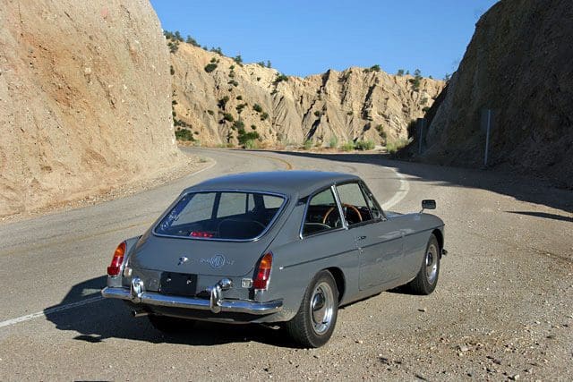 Classic gray vintage car parked on a rugged dirt road between rocky cliffs.