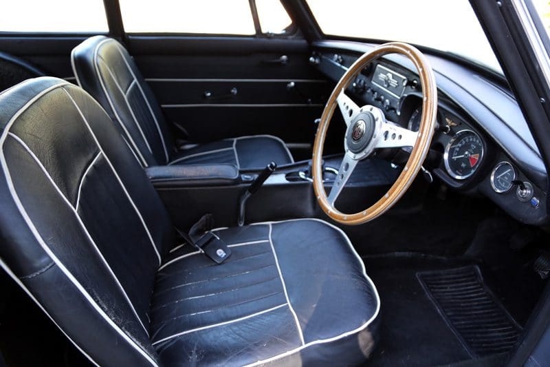 Classic car interior with black seats and wooden steering wheel.