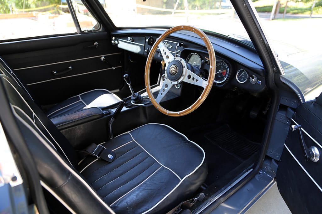 Interior of a classic car with wood-rimmed steering wheel and black leather seats.