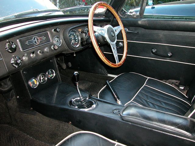Interior of a classic car with wooden steering wheel and manual gear shift.