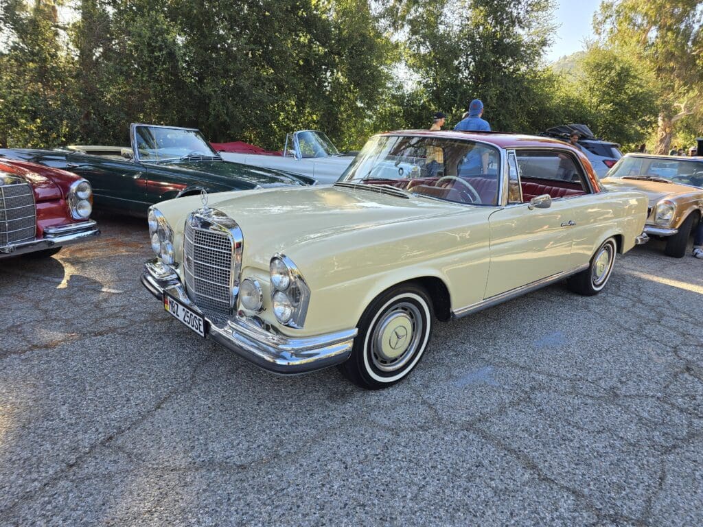 Classic cream-colored Mercedes-Benz convertible parked outdoors beside other vintage cars.