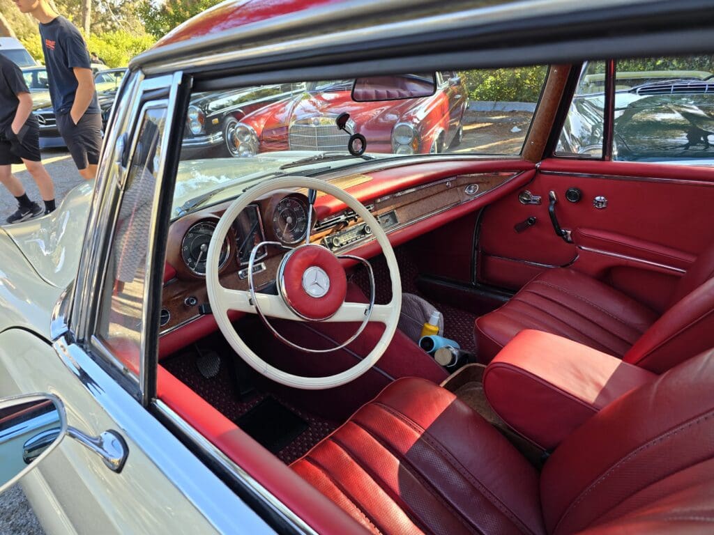 Classic cream-colored Mercedes-Benz convertible parked outdoors beside other vintage cars.