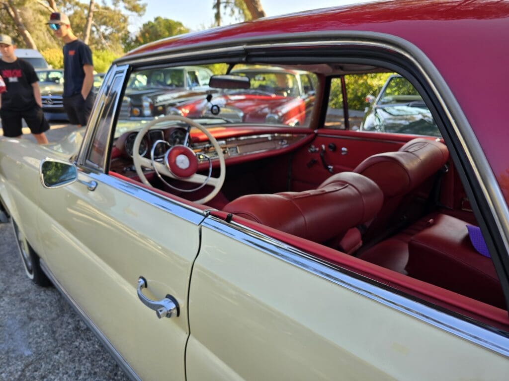 Classic cream-colored Mercedes-Benz convertible parked outdoors beside other vintage cars.
