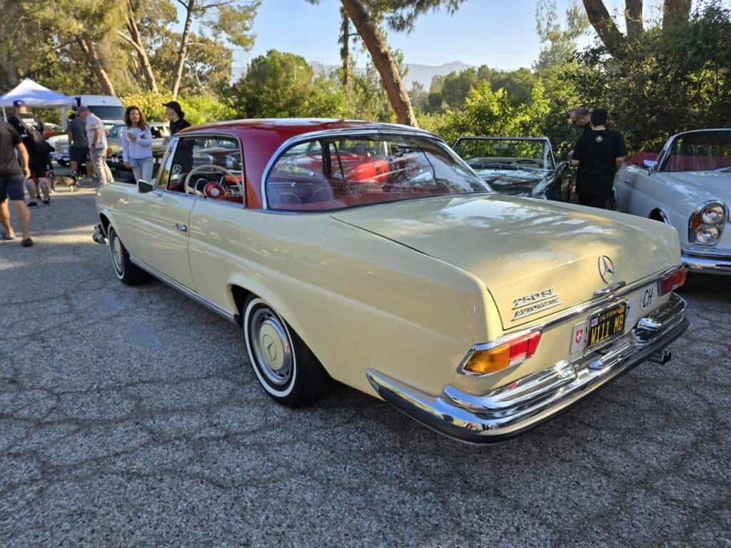 Classic cream-colored vintage car parked outdoors with people nearby.