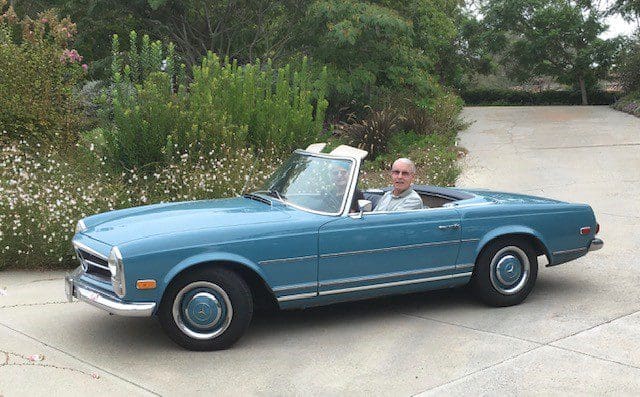 Man driving a vintage blue convertible car on a driveway.