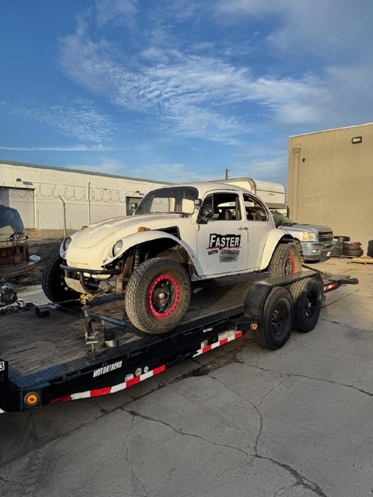 Vintage off-road car on trailer under blue sky.