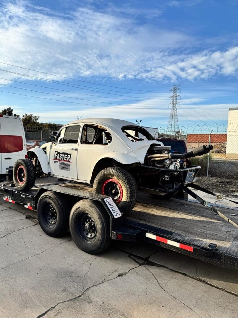 A vintage race car loaded on a trailer under a partly cloudy sky.