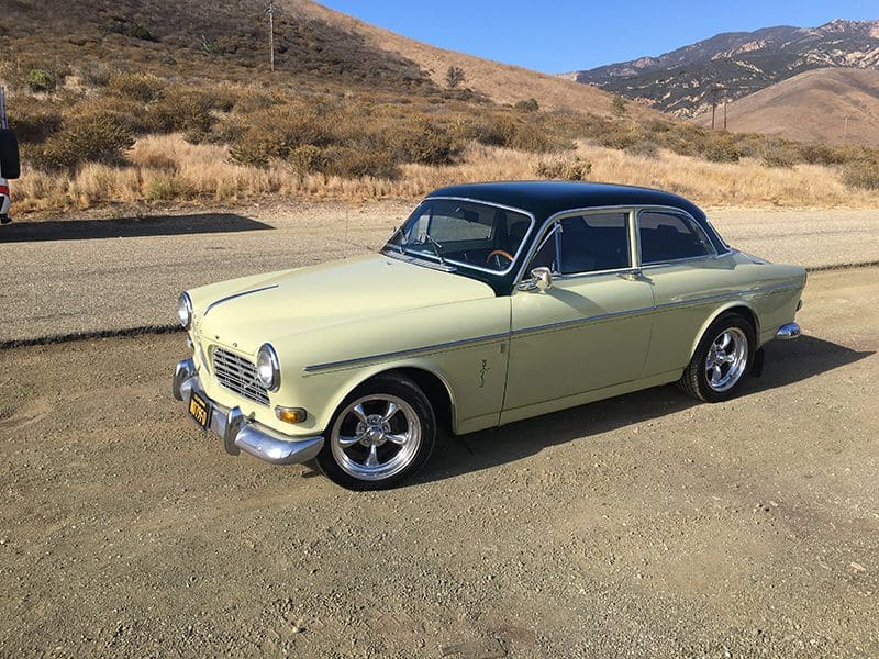 Classic cream-colored vintage car parked on a dirt road.