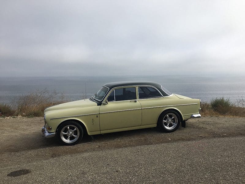 Classic beige vintage car parked on a hill with a cloudy sky.