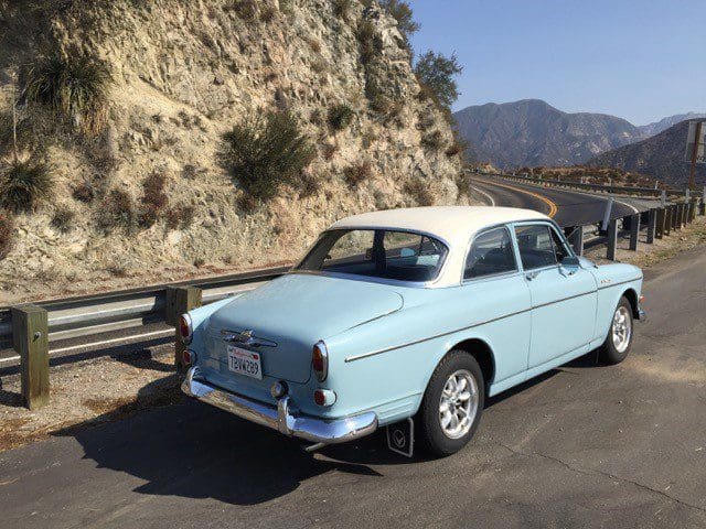 Classic light blue vintage car parked on a mountain road.