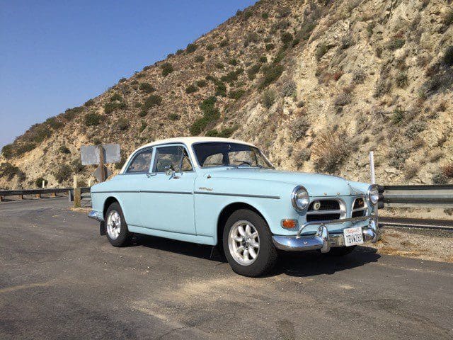 Classic light blue vintage car parked by a rocky hillside.