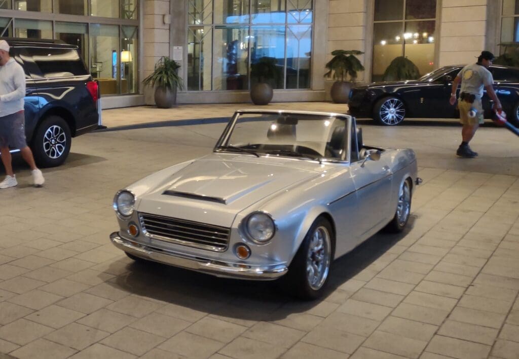 Classic silver convertible car parked on a city street at night.