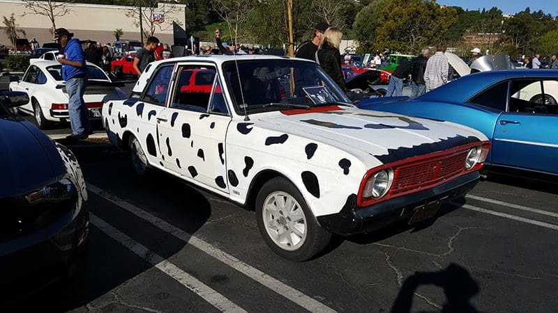 A vintage white car painted with black spots like a Dalmatian.