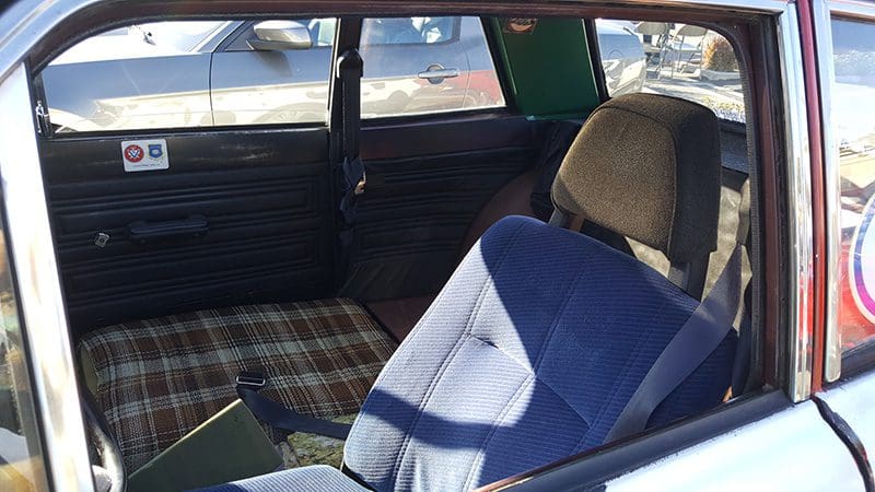 Interior of a vintage car with plaid seats and a blue jacket on the front seat.